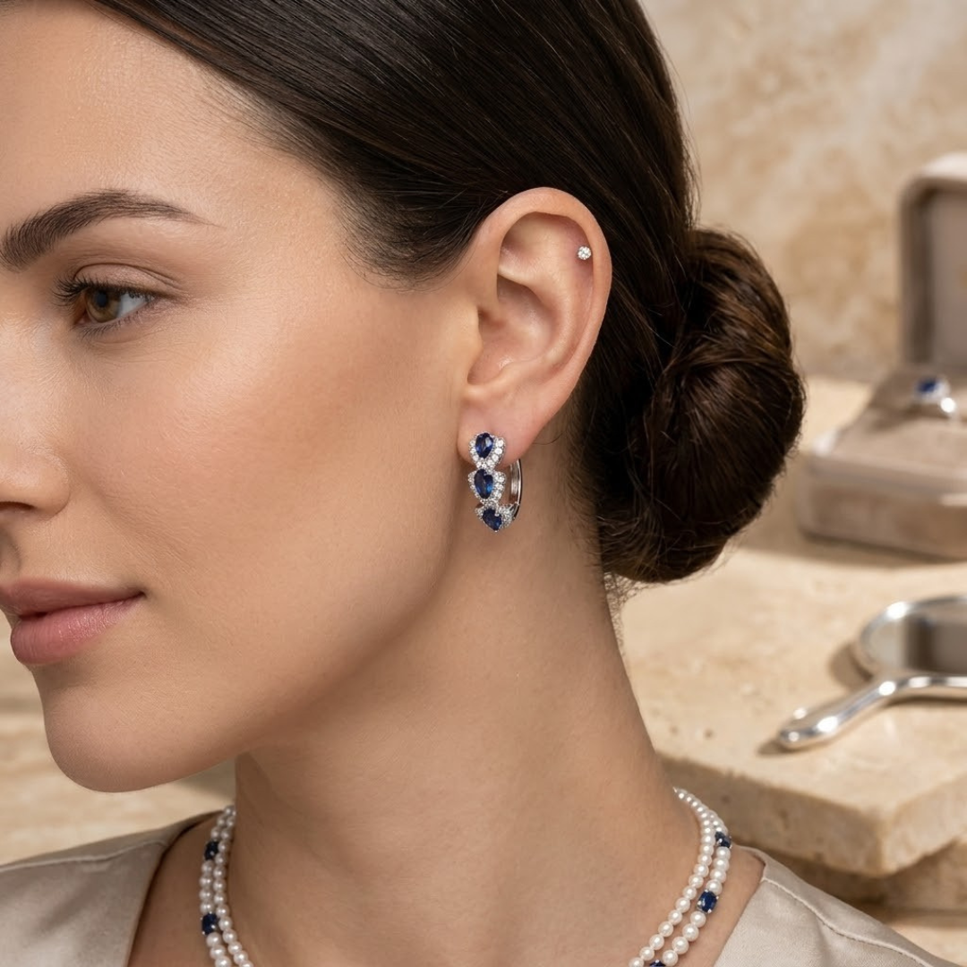 Brincos de argola prateados com halo de safira, detalhes elegantes, da marca Rose & Oliver, visíveis na imagem.