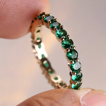 Anel de ouro com esmeraldas em formato de eternidade, da marca Rose & Oliver, exibindo pedras verdes brilhantes e acabamento elegante.