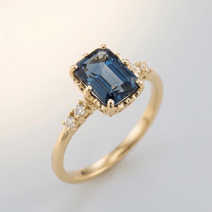 Anel de ouro com safira azul e detalhes em diamante, da marca Rose & Oliver, exibido em fundo neutro.