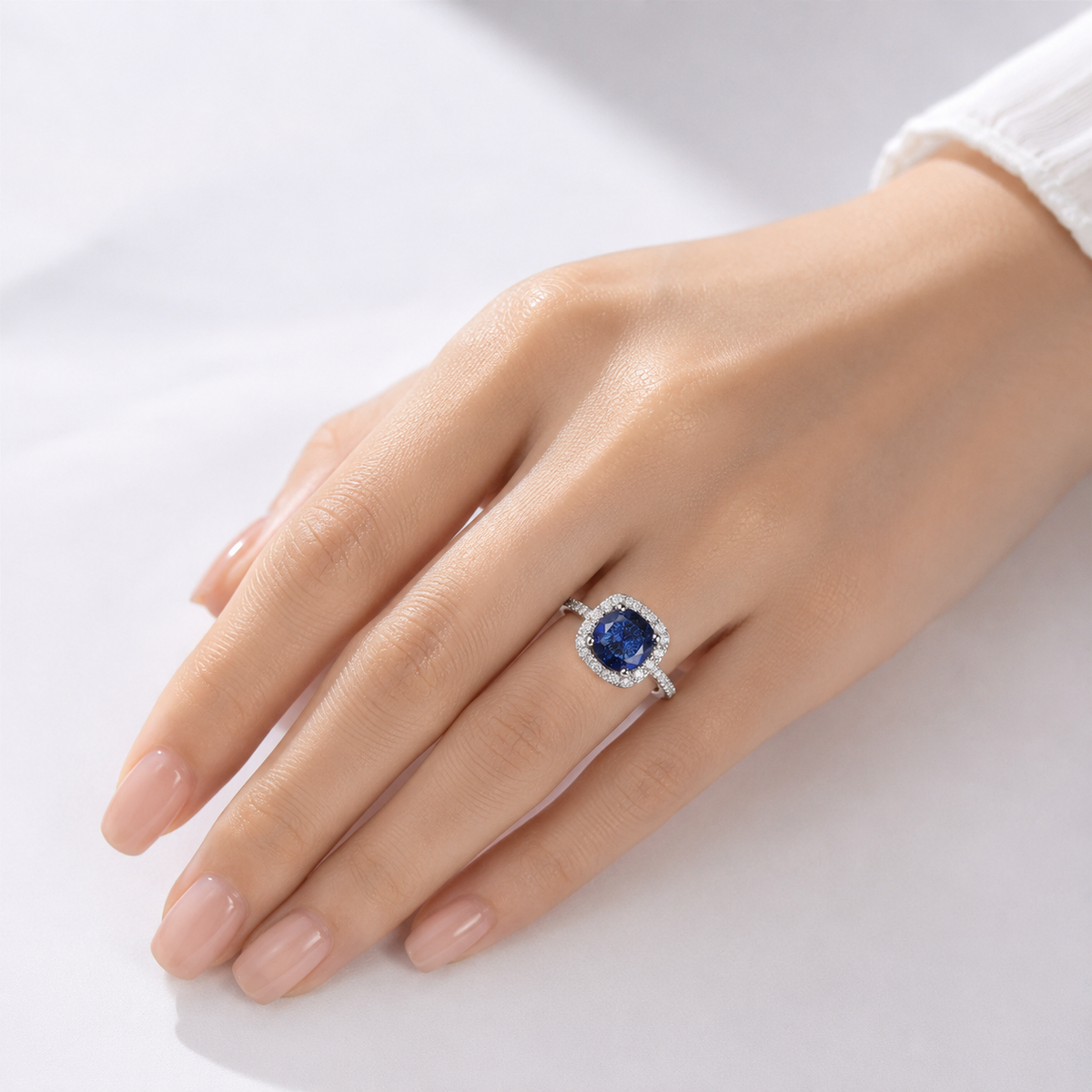 Anel de safira azul em corte cushion com halo de diamantes, da marca Rose & Oliver, exibido na imagem.