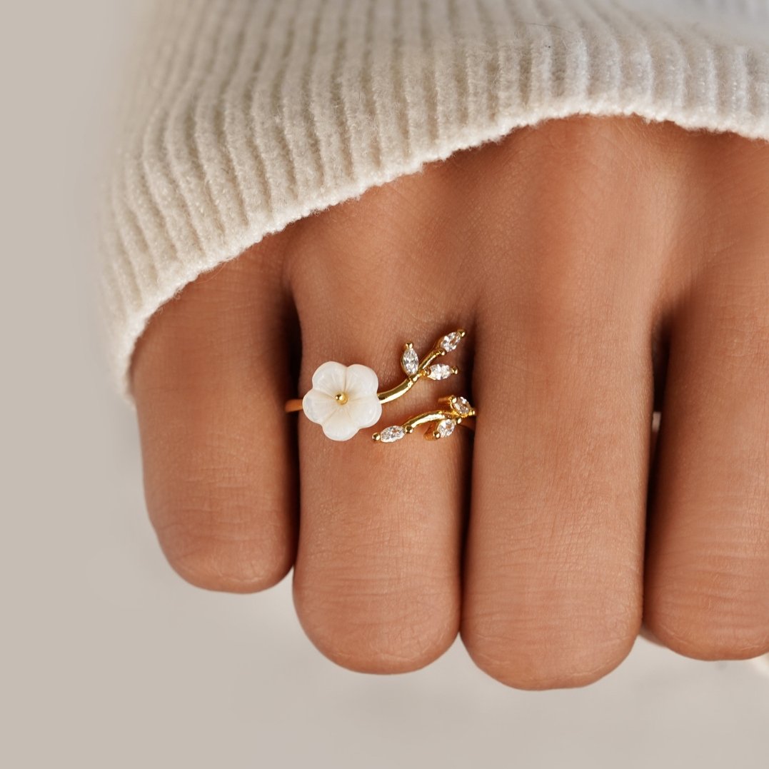 Anel aberto dourado com flor de jardim e folhas delicadas, design floral elegante da marca Rose & Oliver.